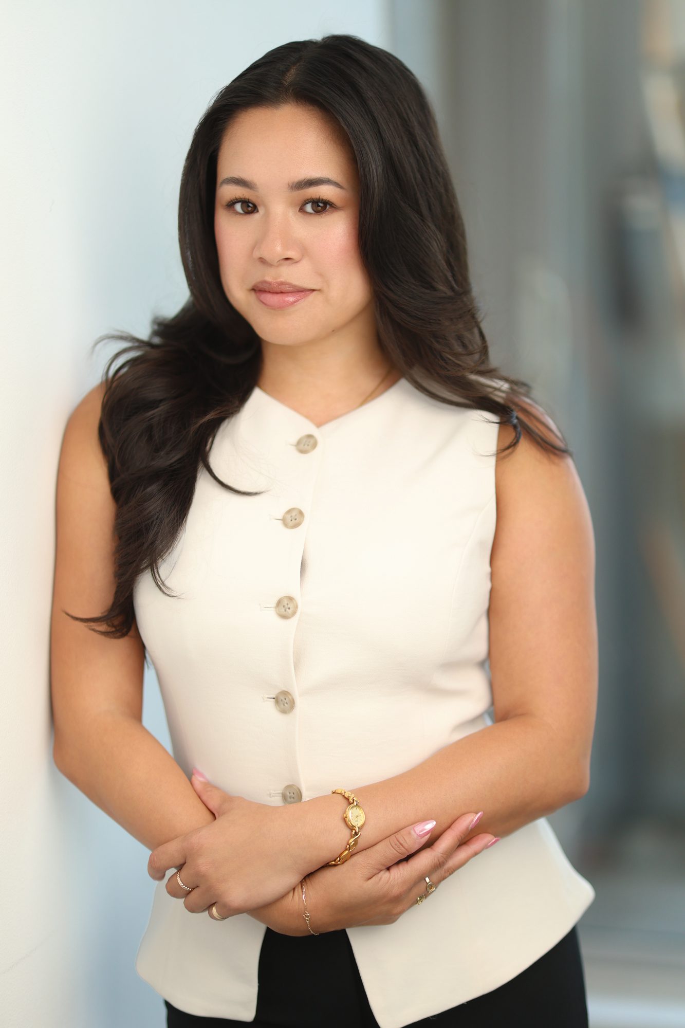 Young woman with long dark hair wearing a white sleeveless top.