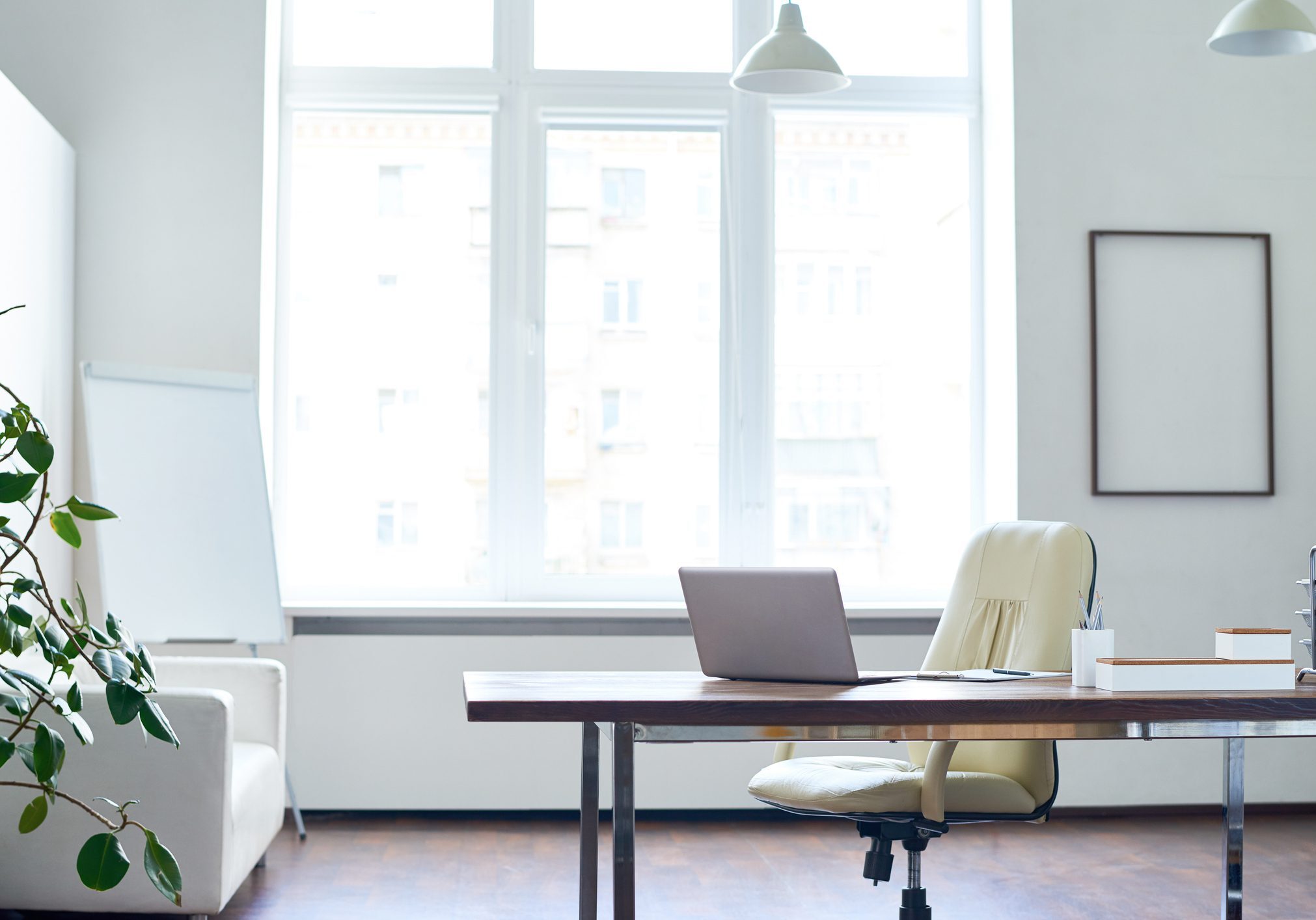 Bright modern office with a desk, laptop, and ergonomic chair by large windows.